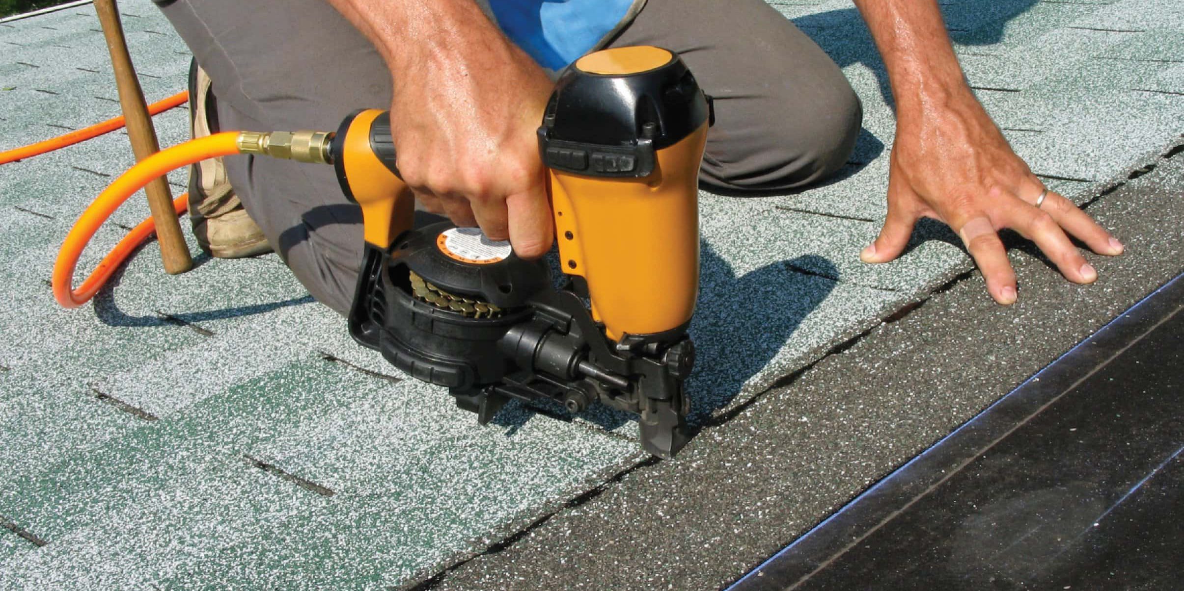 Person using nail gun on roof shingles.
